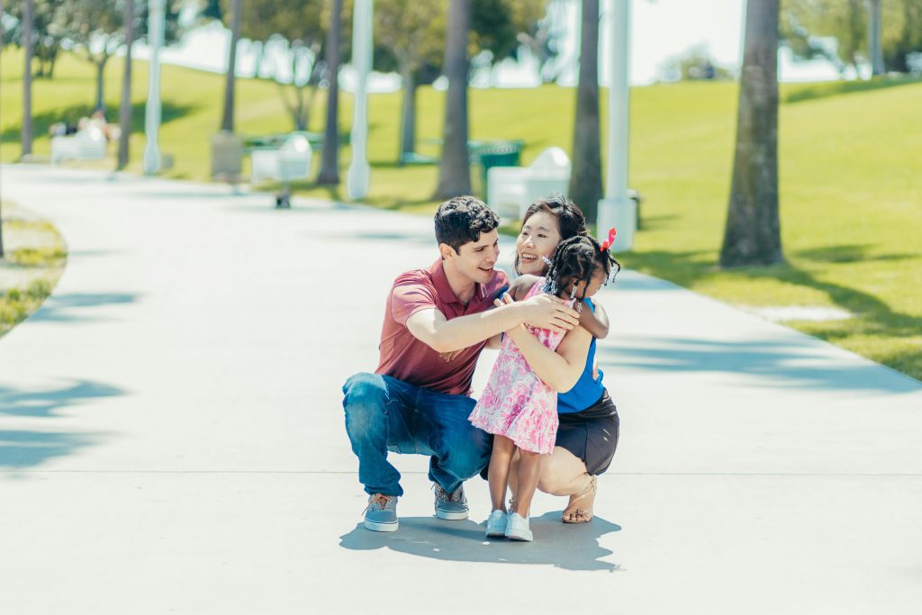 A man and lady sitting on knees - lady hugging a little girl