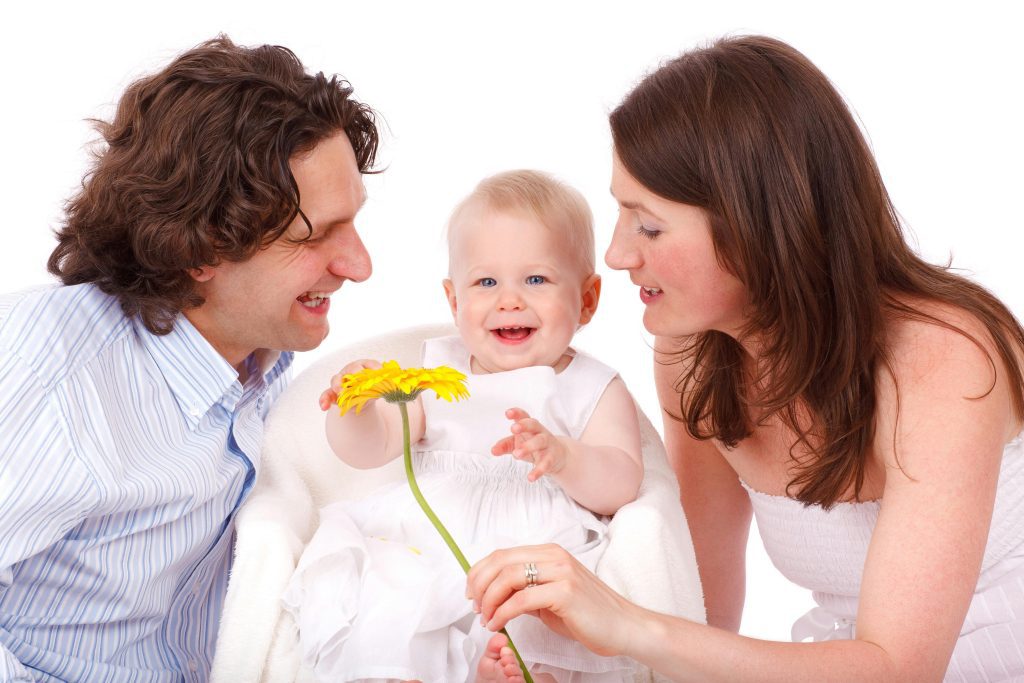 A man is smiling seeing a little kid- a lady giving flower to that little kid- little girl is smiling