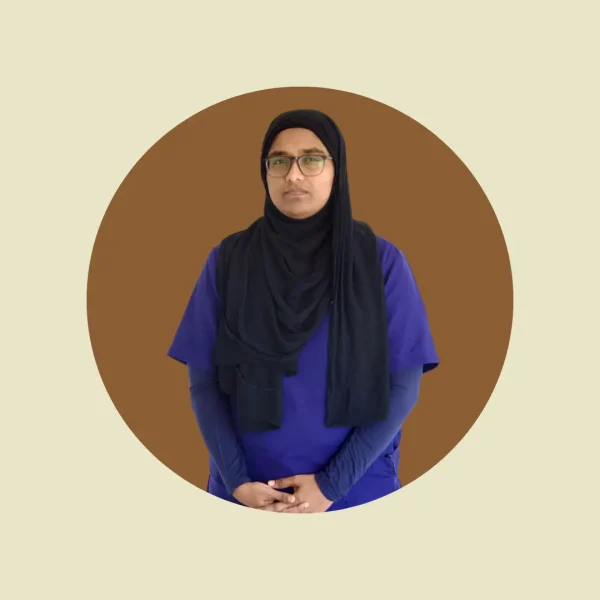 A female healthcare professional wearing a blue medical uniform and a black hijab, posing for a professional portrait against a circular brown background