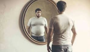 Man looking in a mirror and seeing a larger, altered reflection of himself.