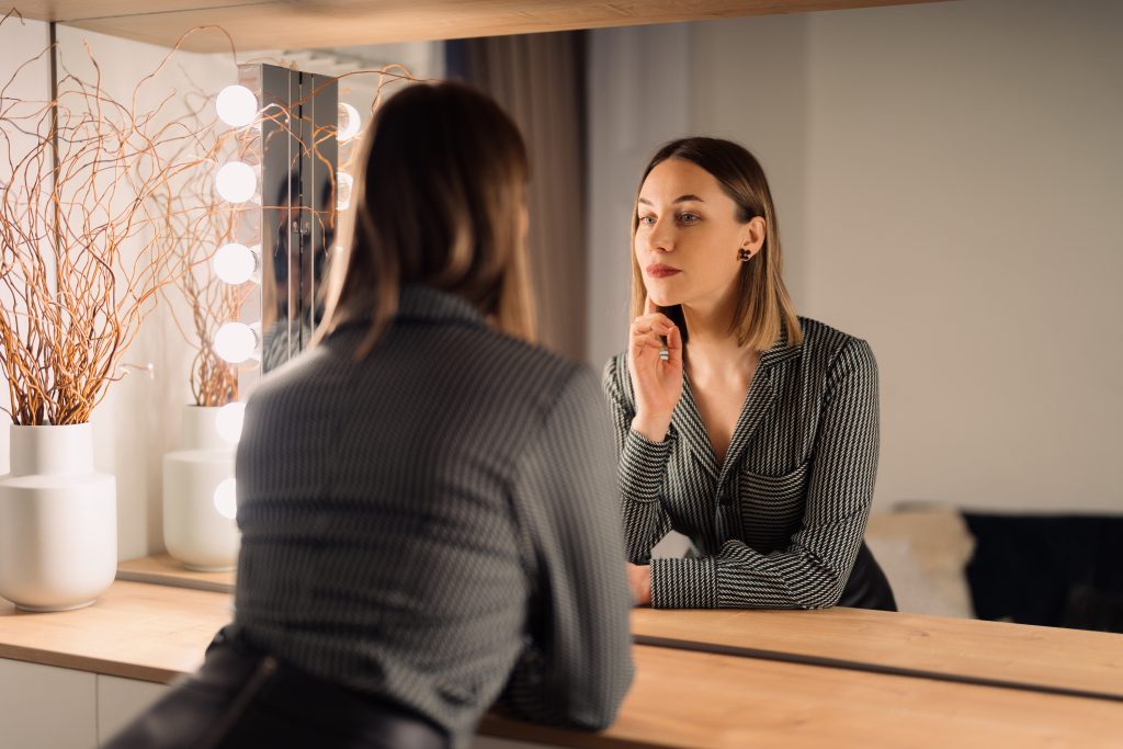 Woman looking at her reflection in a mirror during a mental health counseling session for Body Dysmorphic Disorder (BDD)